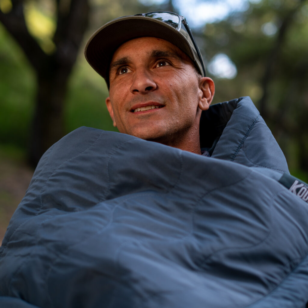 Man enjoying the great outdoors wrapped in The Kodiak Battery Powered Heating Blanket